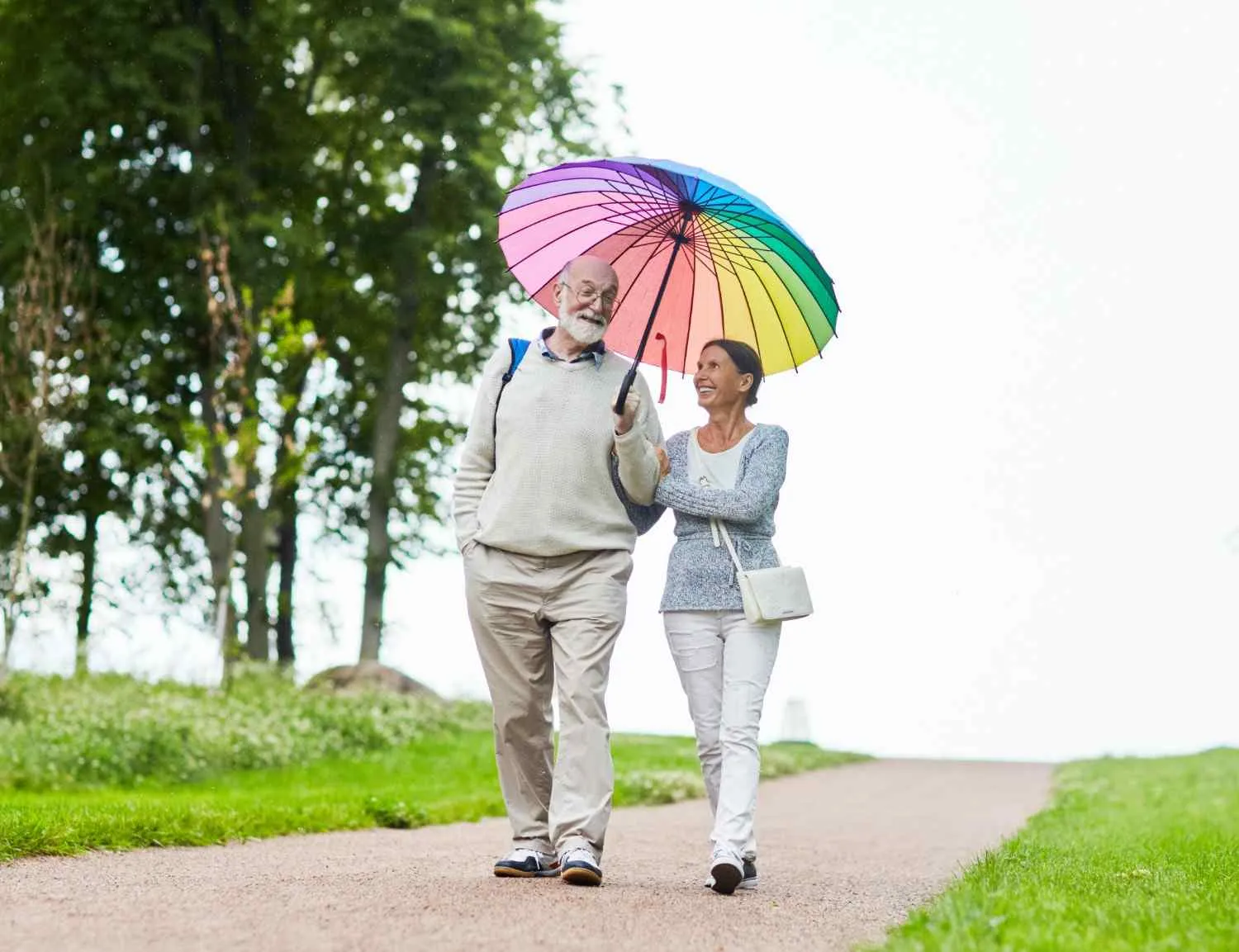 Older couple walking together under an umbrella along a park path